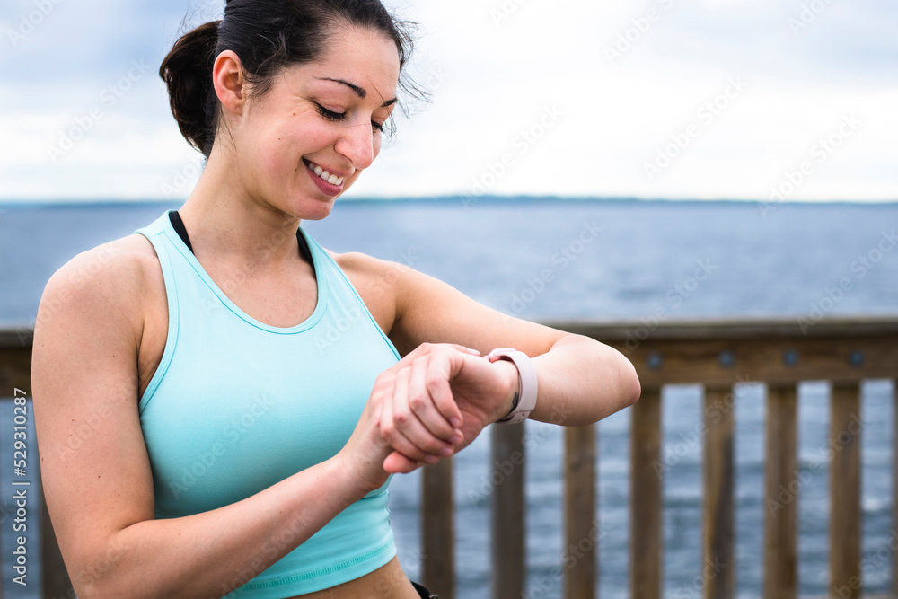 Smiling woman checking time while standing by sea on pier against sky Smiling woman checking time while standing by sea on pier against sky
