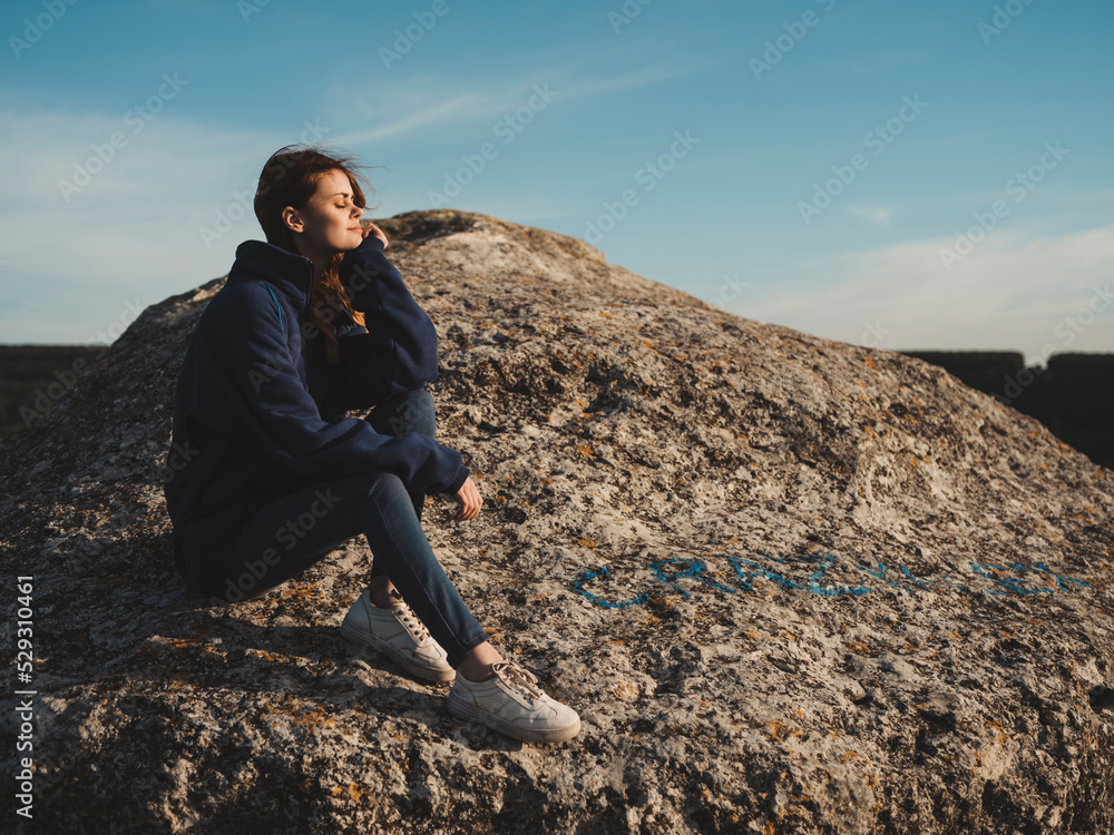 Side view of woman with eyes closed sitting on rock formation against sky during sunny day Side view of woman with eyes closed sitting on rock formation against sky during sunny day