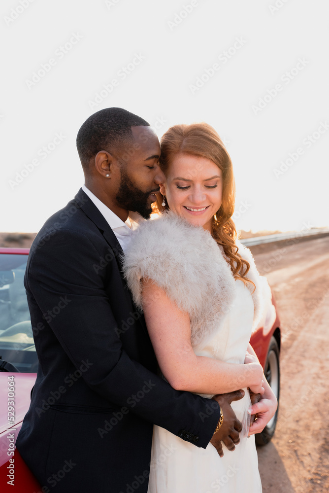 Side view of newlywed couple romancing while standing by convertible against clear sky Side view of newlywed couple romancing while standing by convertible against clear sky