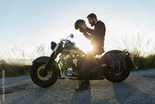 Side view of male biker wearing crash helmet while sitting on motorcycle against clear sky during sunset photo
