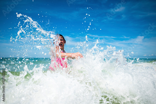 Playful girl splashing water in sea against sky during sunny day