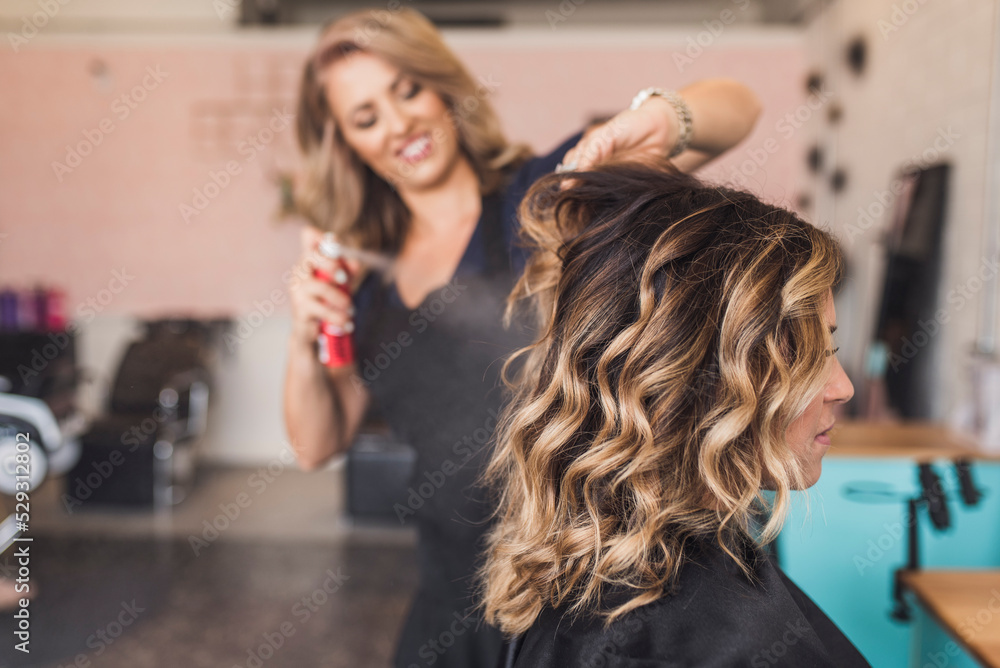 Hairdresser spraying beauty product on customer's wavy hair in salon Hairdresser spraying beauty product on customer's wavy hair in salon