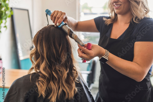Midsection of hairdresser using curling tongs on customer's hair in salon photo