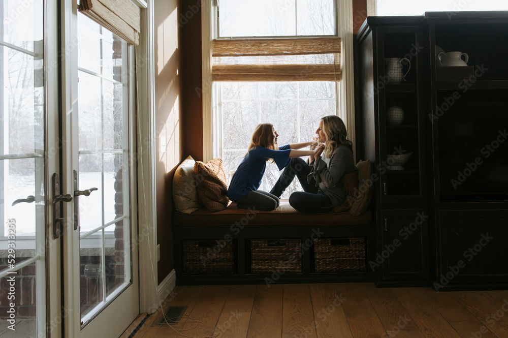 Side view of mother and daughter playing by window at home Side view of mother and daughter playing by window at home