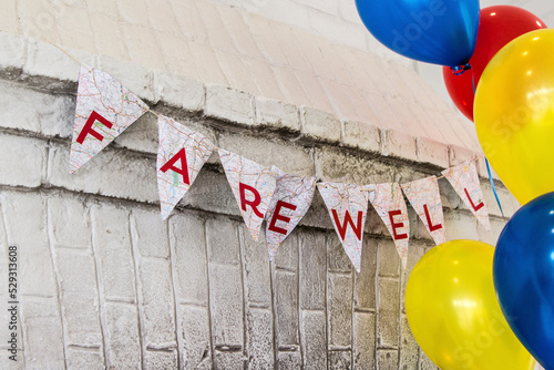 Farewell text on buntings by colorful helium balloons hanging against wall photo