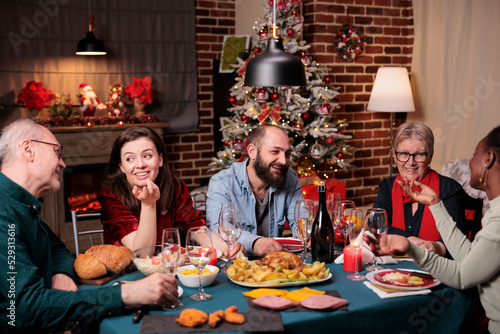Big diverse family celebrating christmas  talking at festive dinner table  eating traditional winter holiday food. Xmas celebration at beautiful decorated place  fir tree  fireplace on background