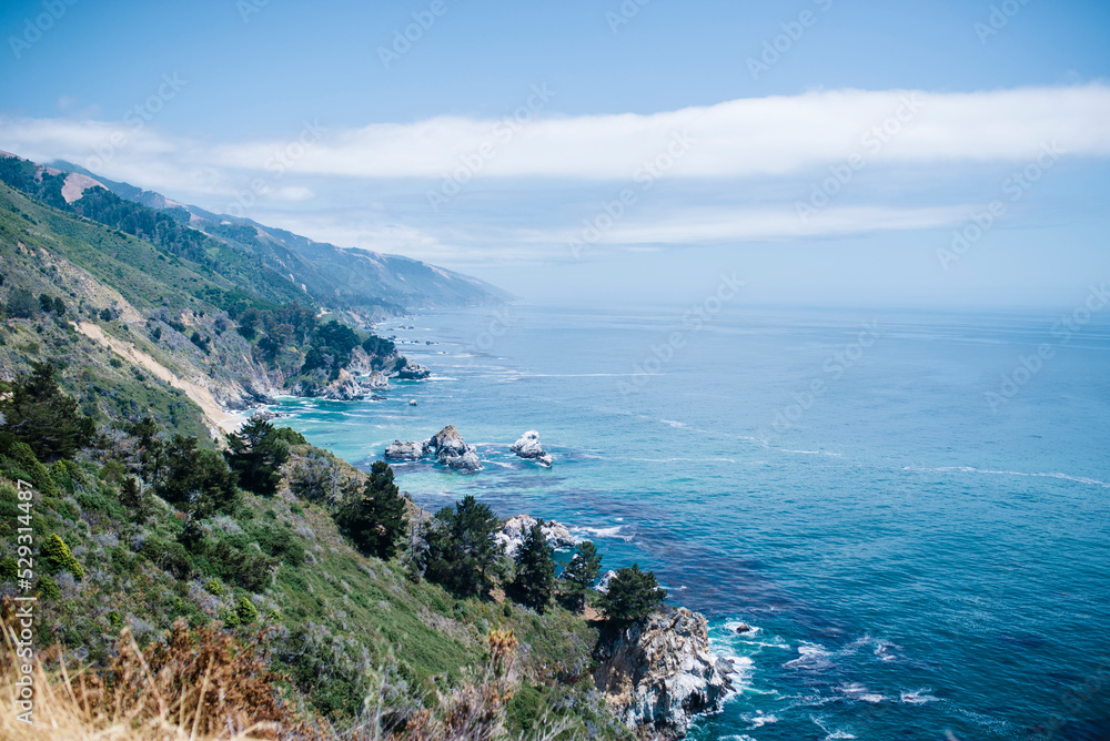 Scenic view of sea by mountain against cloudy sky during sunny day Scenic view of sea by mountain against cloudy sky during sunny day