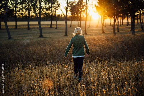 Rear view of girl walking amidst plants on field during sunset