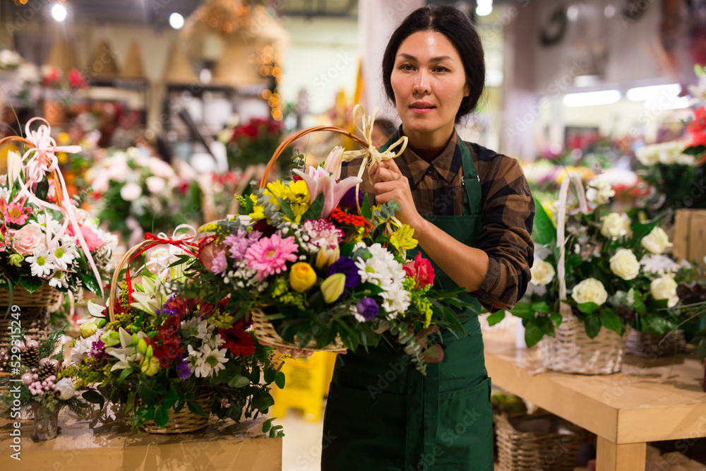 Female florist in apron carrying basket with flowers while working in salesroom.