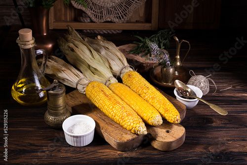 Baked and grilled cobs of corn on wooden cutting board