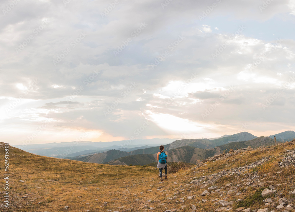 Rear view of female hiker with backpack looking at view while standing on mountain against cloudy sky during sunset Rear view of female hiker with backpack looking at view while standing on mountain against cloudy sky during sunset