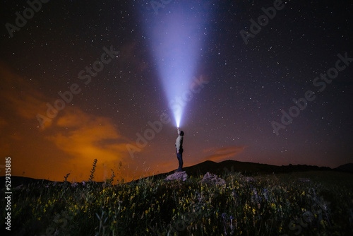 Side view of man holding illuminated flashlight while standing on hill against star field at night photo
