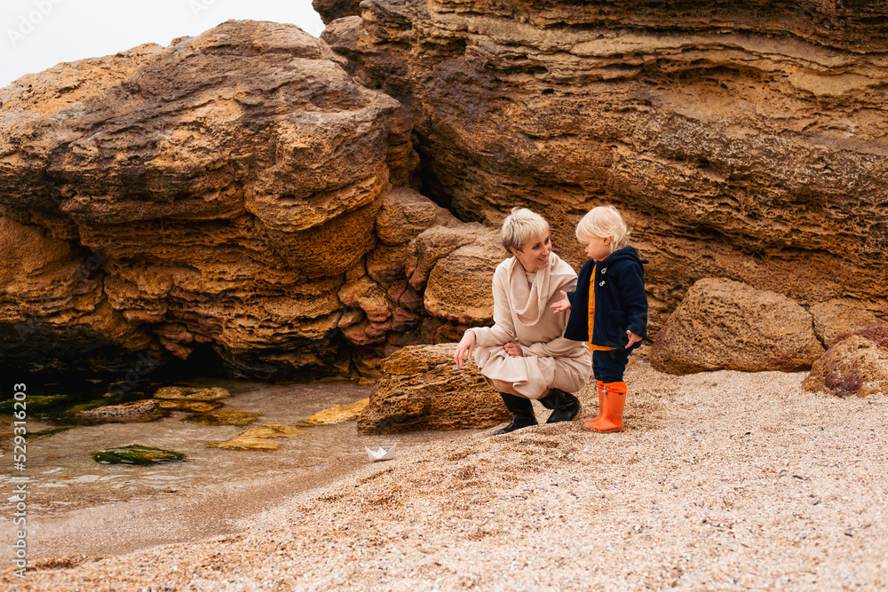 mother and son playing with paper boat on beach near sea in autumn beach