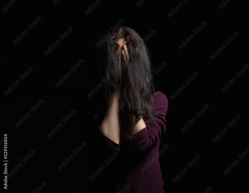 Woman covering face with hands while standing against black background Woman covering face with hands while standing against black background
