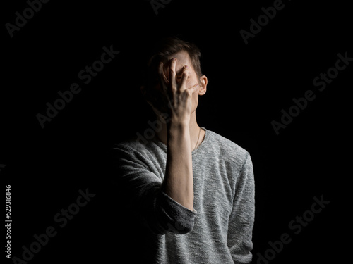 Man covering face with hand while standing against black background