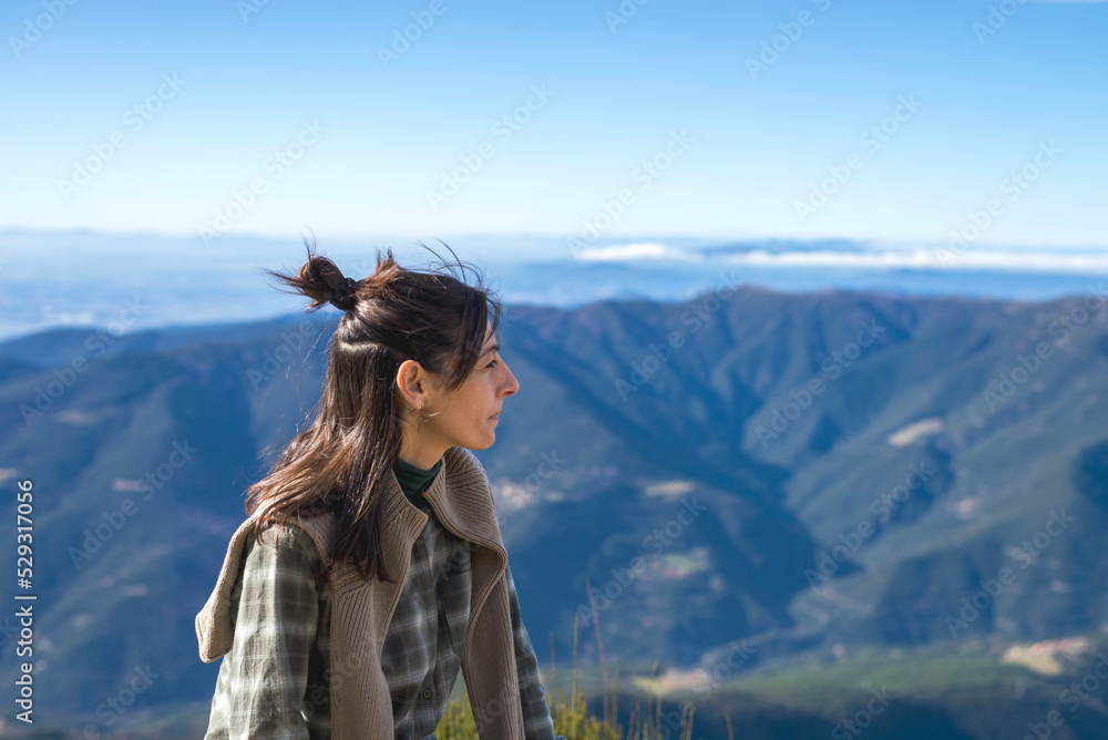 Woman looking at view while sitting on mountain against clear blue sky during sunny day Woman looking at view while sitting on mountain against clear blue sky during sunny day
