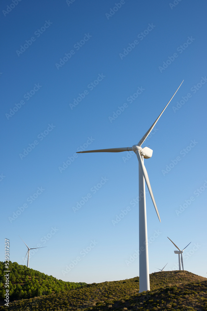 Low angle view of windmills on field against clear blue sky during sunny day Low angle view of windmills on field against clear blue sky during sunny day