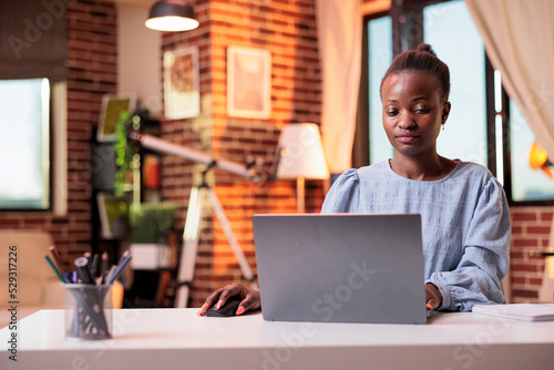 Successful businesswoman typing on laptop and working in modern home office. Smiling female freelance copywriter using portable computer in coprorate workspace with beautiful warm sunset light photo