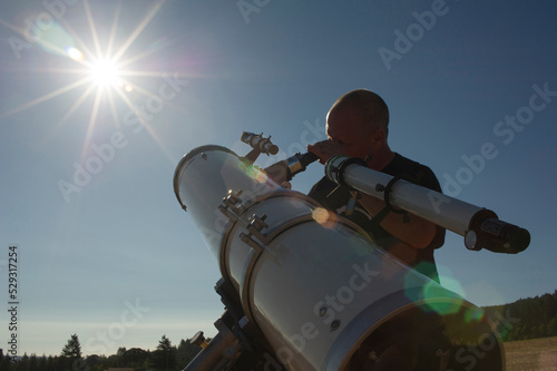 Low angle view of astronomer looking bright sun through telescope against clear sky during sunny day photo