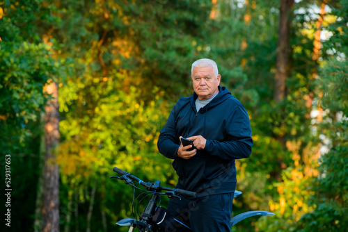 an elderly sports man uses a smartphone while walking on a bicycle © serhii