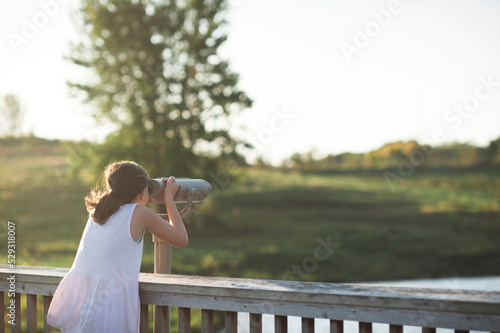 Preteen girl looks into grassy field through viewing scope photo