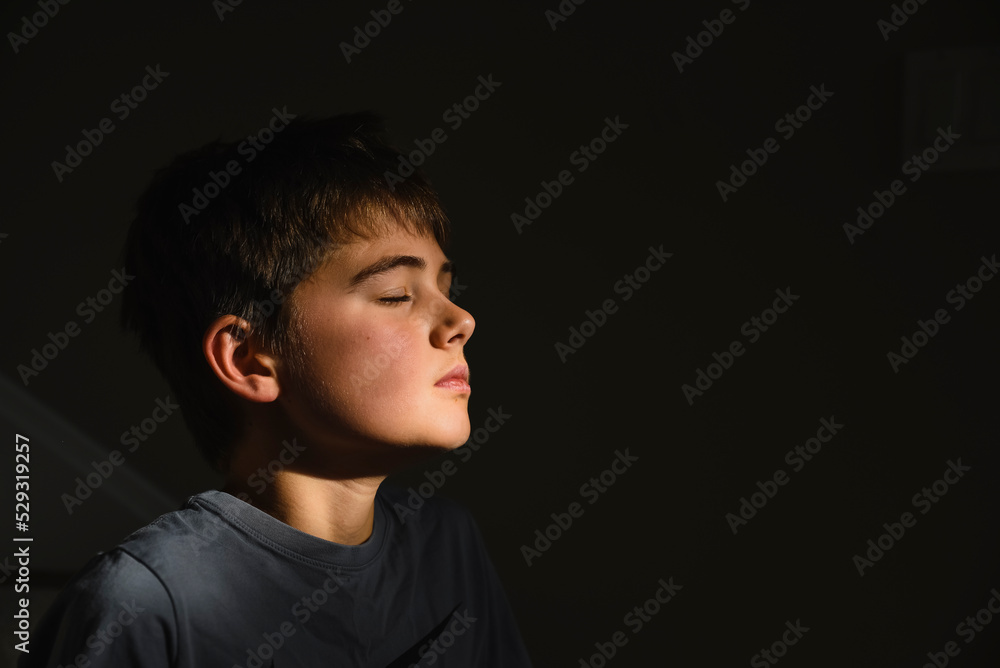 Close up of adolescent boy's face in patch of sun with his eyes closed Close up of adolescent boy's face in patch of sun with his eyes closed