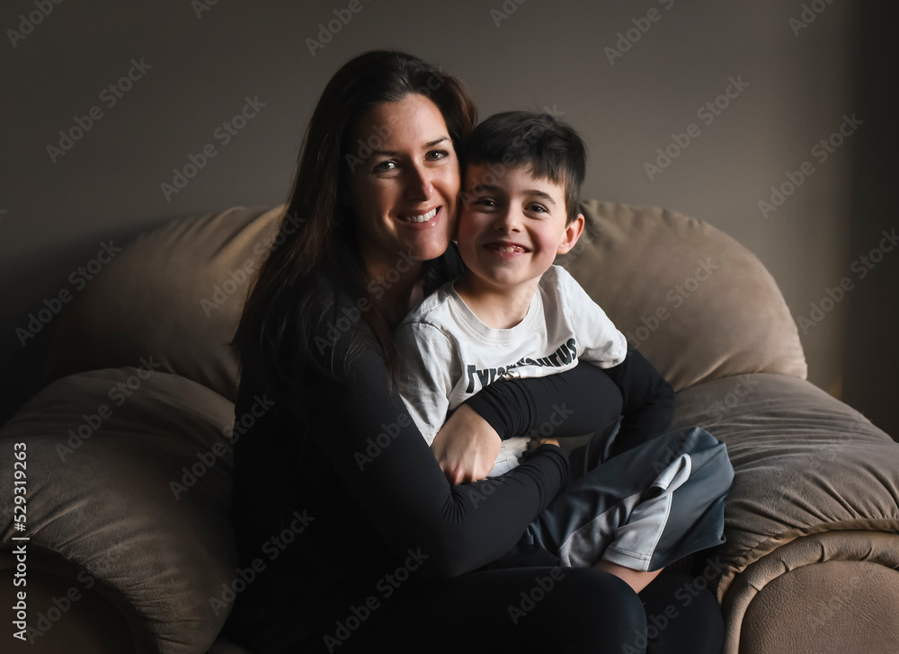 Young boy sitting on mother's lap in chair beside a window. Young boy sitting on mother's lap in chair beside a window.