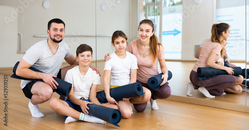 Family portrait of kids and parents with yoga mats in gym.