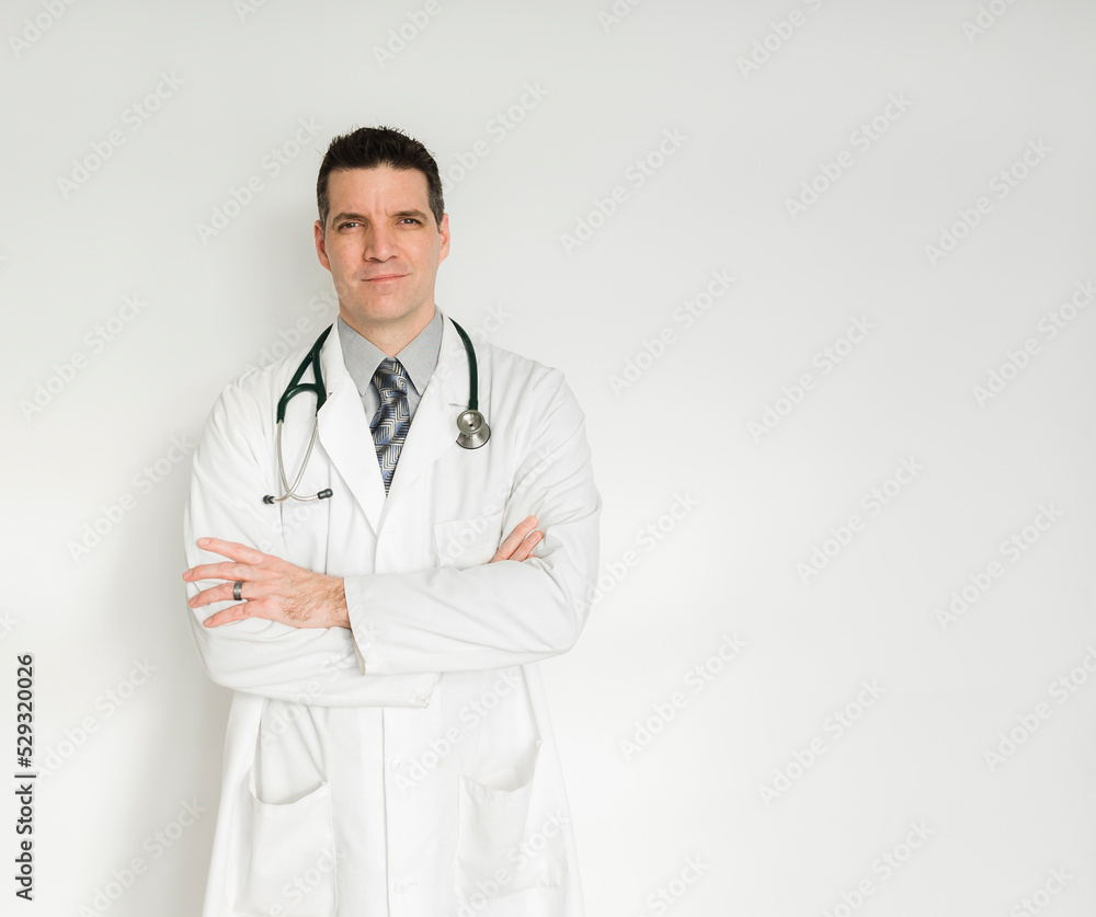 Doctor in white coat standing with arms folded against white backdrop. Doctor in white coat standing with arms folded against white backdrop.