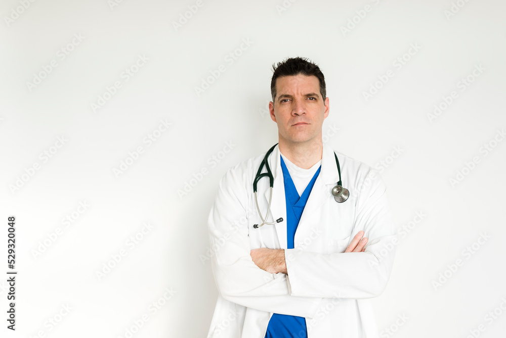 Medical doctor in white coat and scrubs standing with arms folded. Medical doctor in white coat and scrubs standing with arms folded.
