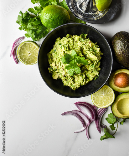 Close up of bowl of guacamole and it's ingredients on a white counter. photo
