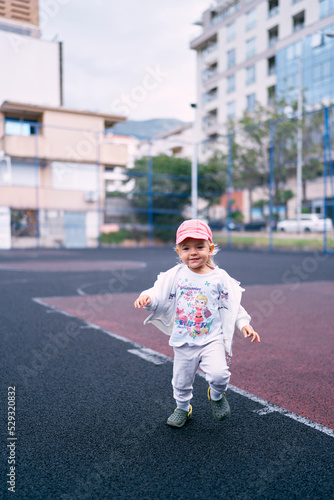 Little girl in a tracksuit walks on the sports ground. High quality photo