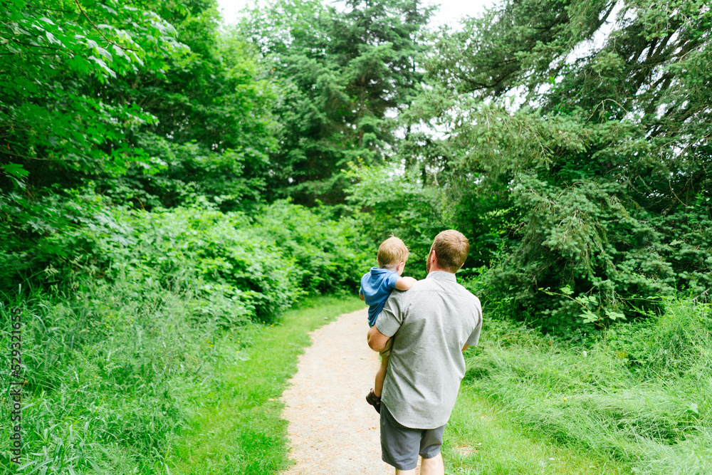 Rear view of a dad holding a son while hiking down a path Rear view of a dad holding a son while hiking down a path