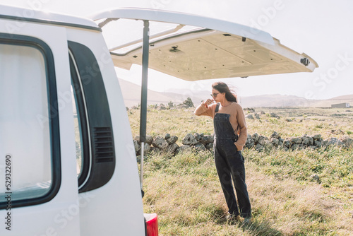 A woman brushing teeth outdoors besides a camper van photo