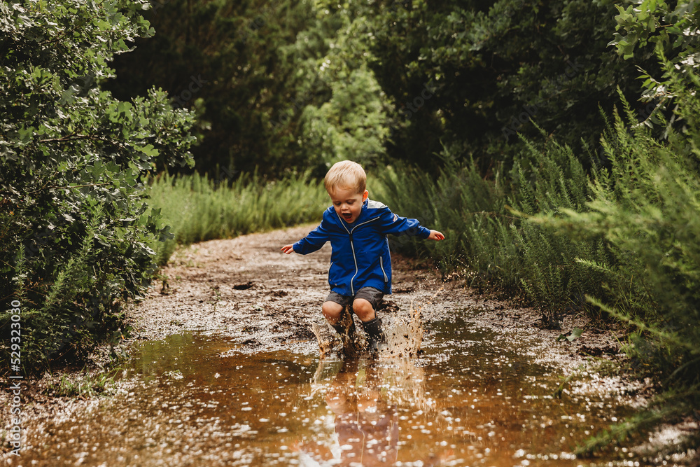 Young boy jumping into muddy puddle and making a splash Young boy jumping into muddy puddle and making a splash