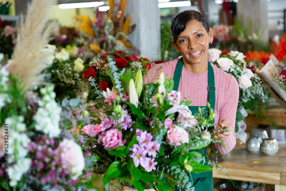 Smiling latino american woman flower seller prepares a luxury bouquet at flower shop