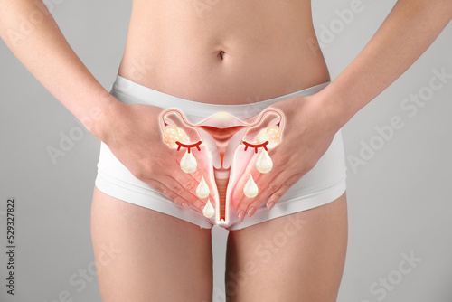 Woman holding hands on her belly and illustration of female reproductive system against light grey background, closeup. Vaginal yeast infection photo