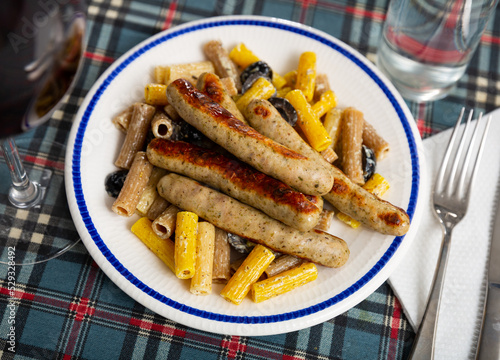 Delicious rigatoni with olives in creamy sauce served with roasted sausages. Italian dish..