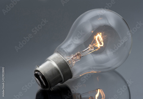 Stampa su tela Domestic bayonet fitting light bulb with glowing filament lying on a grey reflec