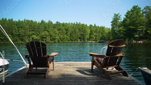 Two empty Muskoka chairs sit at the end of a dock looking out at the water on a calm, beautiful summer day. photo