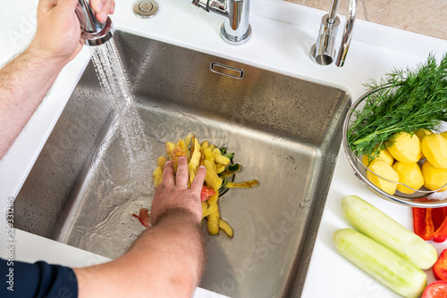 A hand shoves food waste into a disposer hole in the kitchen sink photo