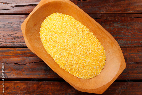 Raw cornmeal flour used in polenta, in wooden bowl over rustic wooden table