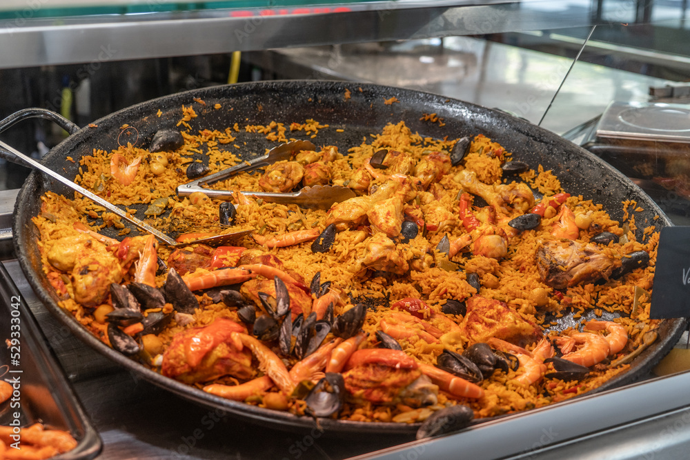 Paella with yellow saffron, seafood, clams prepared at a Spanish market on a traditional large black paella pan
