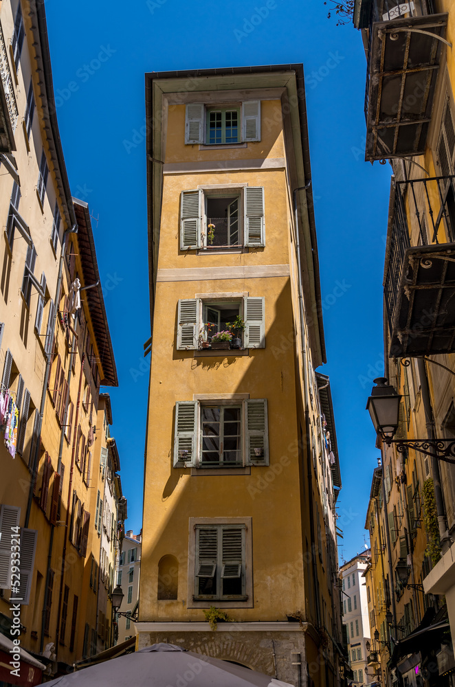 Flat iron building with yellow walls, windows with green wooden shutters in Nice old town