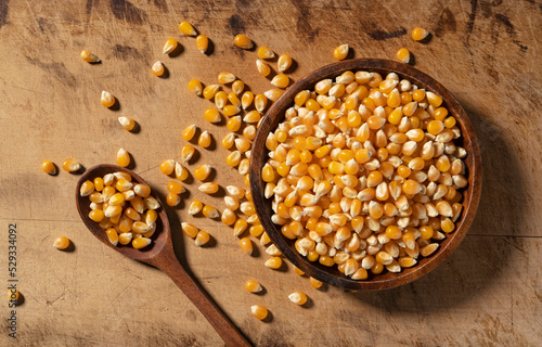 Dried corn kernels and wooden spoon in wooden bowl placed on wooden background.