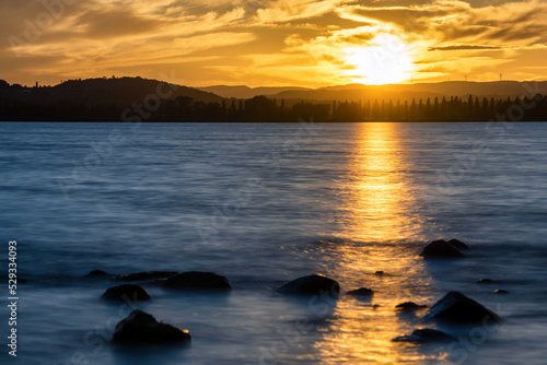 Golden sunset at Lake Constance with stones in the foreground and clouds in the sky