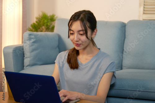 夜のリビングでノートパソコン使う女性
