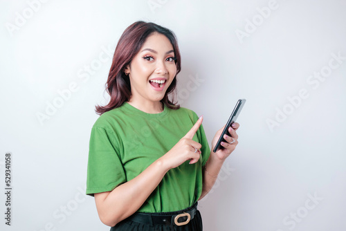 A portrait of a happy Asian woman is smiling and holding her smartphone wearing a green t-shirt isolated by a white background