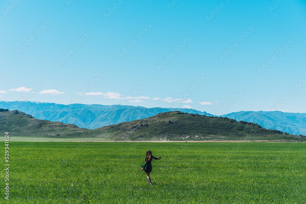 Girl in green dress with hat in her hands walks along feather grass field