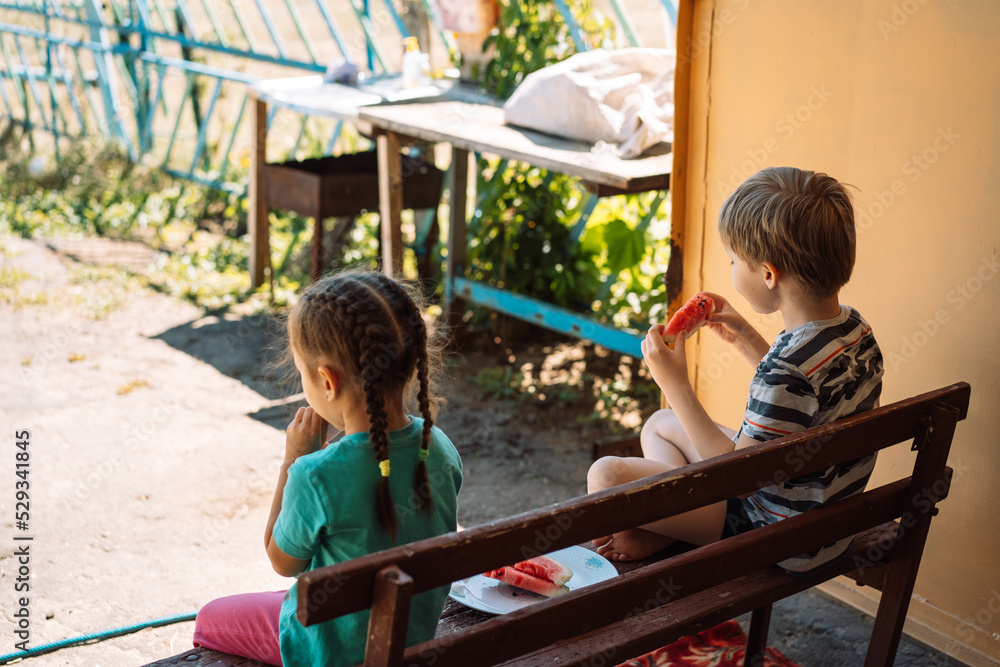 Obraz premium Children sitting on a bench eat watermelon.